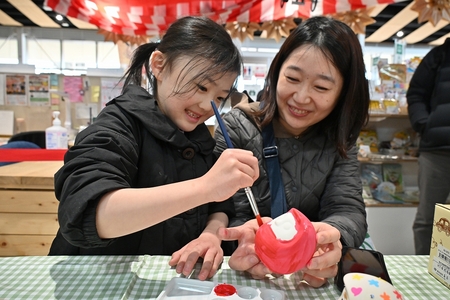 お母さんが手に持っている白いだるまに、筆で赤色を塗る子どもの様子。