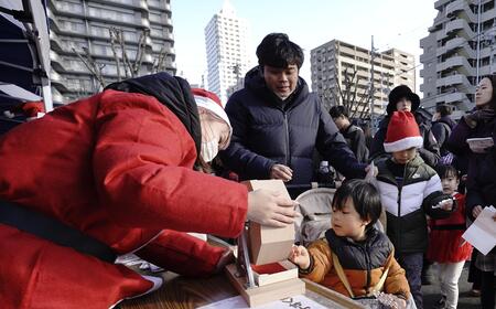 ガラポン抽選会で、福引器を回している、ベビーカーに乗った男の子の様子。サンタが様子を見守っている。