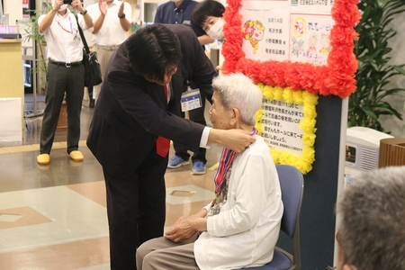 市長が堀江ハツさんに記念の金メダルをかける様子